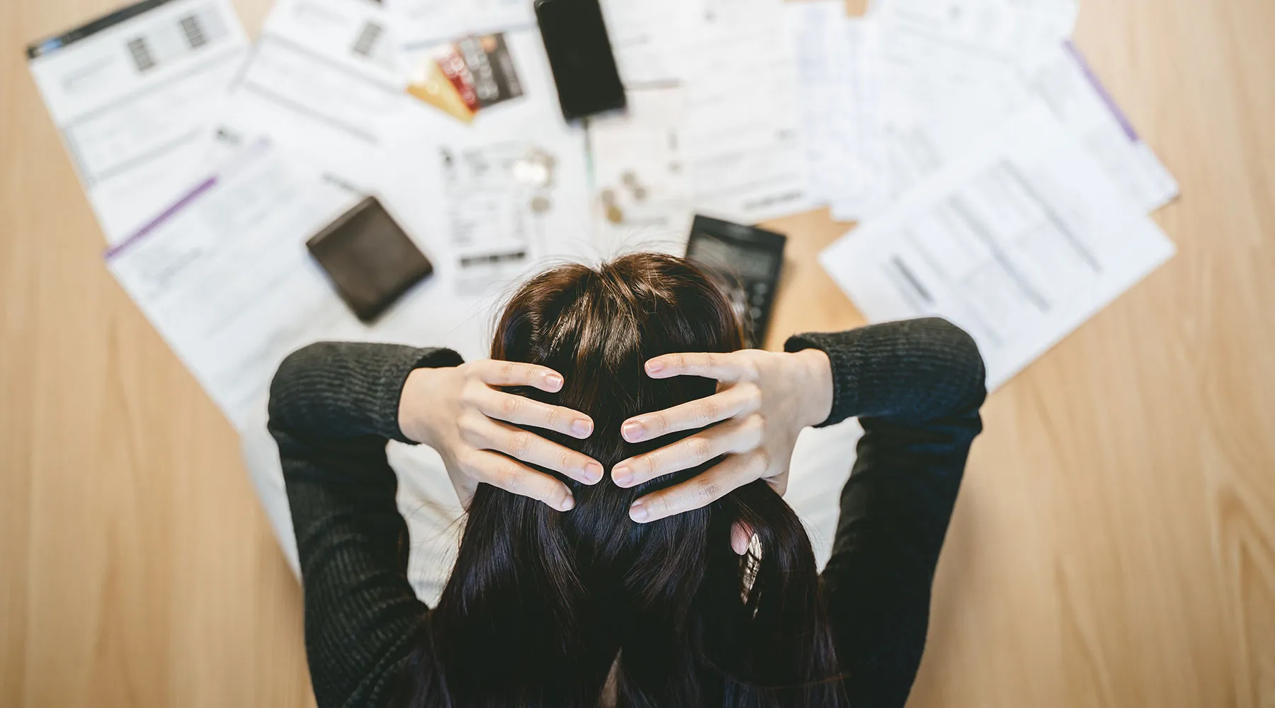 Someone with their head in their hands above a table of scattered bills