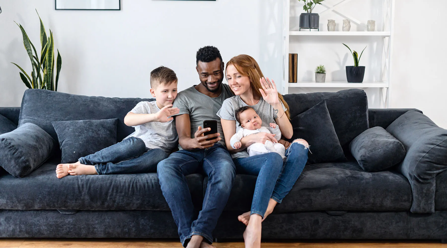 A young family on their sofa waving during a video call