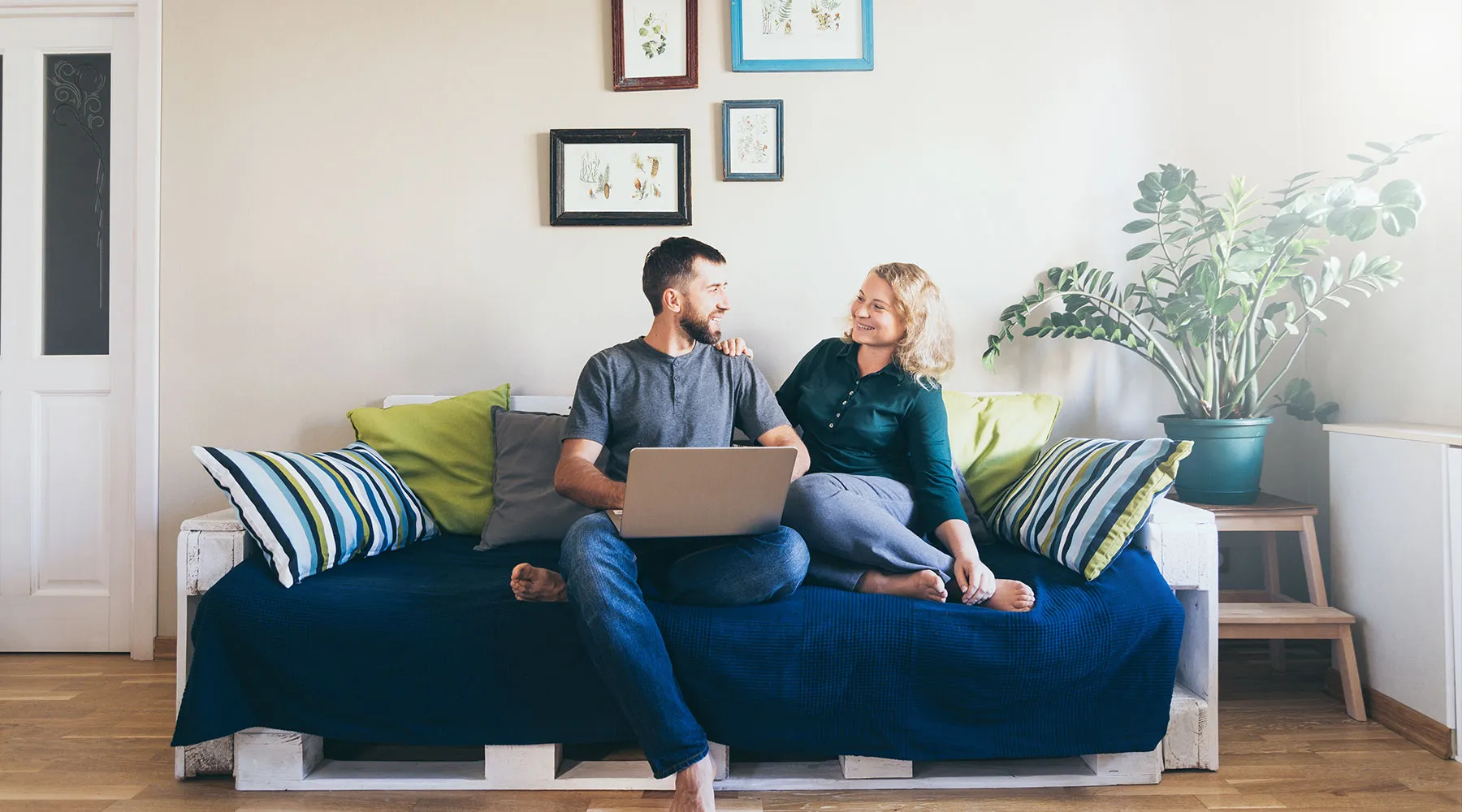 A relaxed couple on their sofa reviewing paperwork on a laptop