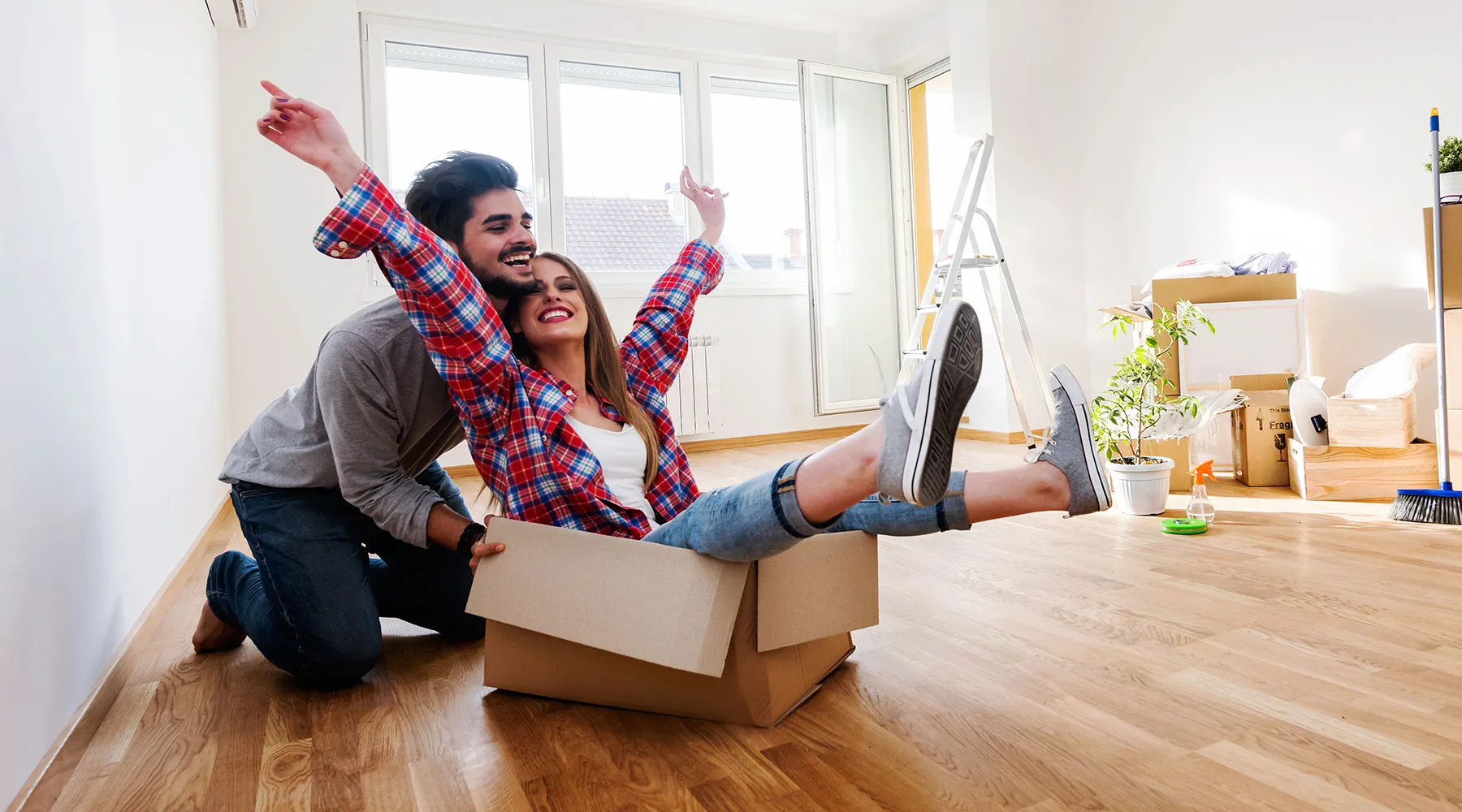 A couple celebrating in their empty new home, one of them sitting in a moving box